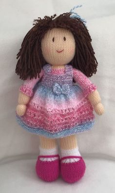 a knitted doll with brown hair wearing a pink and blue dress on a white background