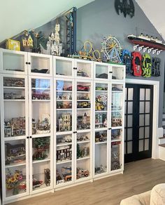 a room filled with lots of toy cars and toys on top of white shelves next to a couch