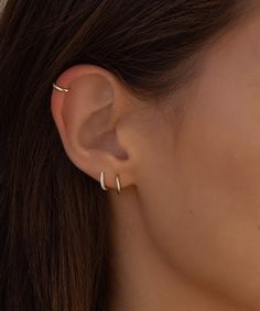 a close up of a woman's ear with two small diamond hoop earrings on it