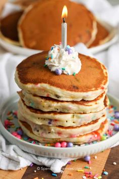 a stack of pancakes with a lit candle on top and sprinkles around it