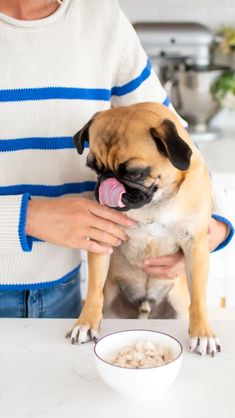 a woman holding a dog in her lap while eating food from a bowl on the counter