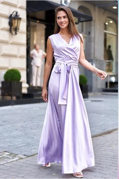 a woman in a long purple dress is walking down the street with her hand on her hip