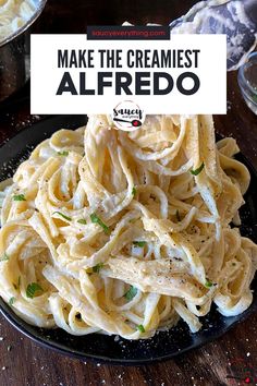 a black plate topped with pasta on top of a wooden table