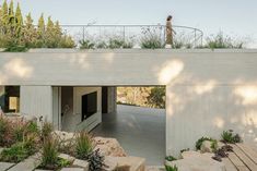 a person walking across a bridge over some rocks and plants on top of the building