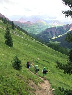 three people hiking up a grassy hill with mountains in the background