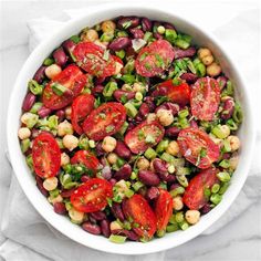 a white bowl filled with beans, tomatoes and other vegetables on top of a table