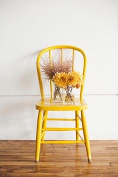 a yellow chair with flowers in it sitting on a wooden floor next to a white wall