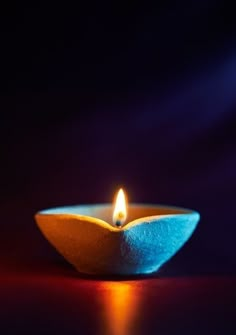 a lit candle sitting on top of a blue bowl with red and yellow lights in the background