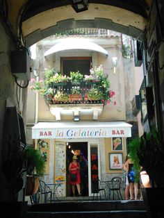 two women standing in the doorway of a bar with potted plants on the balcony