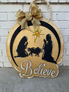 a wooden sign with the words believe and a nativity scene on it, hanging against a brick wall