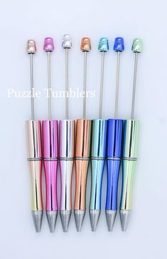 six different colored metal pens lined up next to each other on a white surface with the words puzzle tumblers written below them