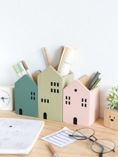 three small houses sitting on top of a wooden desk next to a pen and paper