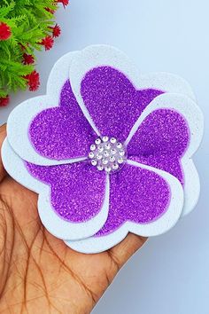 a hand holding a purple and white flower brooch