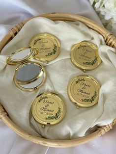 four personalized compact mirrors in a basket on a white cloth with flowers behind them