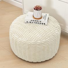 a white round ottoman sitting on top of a hard wood floor next to a potted plant