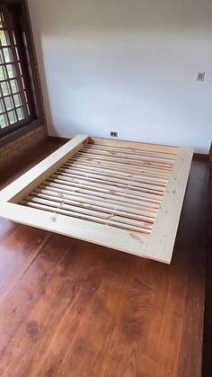 a wooden bed frame sitting on top of a hard wood floor next to a window