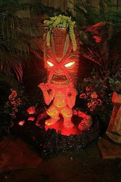 a statue is lit up in the dark with red lights and green plants around it