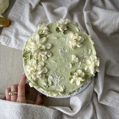 a cake with white flowers on it being held by someone's hand over a blanket