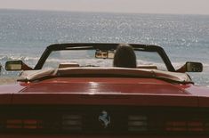 a woman driving a red convertible car on the beach with ocean in the back ground