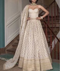 a woman in a white and gold gown standing next to a stair case with her hands on her hips