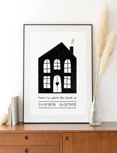 a black and white poster with a house in the window on top of a dresser