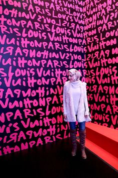 a woman is standing in front of a wall with letters on it and wearing a white coat