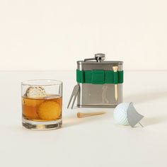 a shot glass with an ice cube and golf tees next to a flask