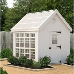 a small white shed with a window on the side and plants growing in the front