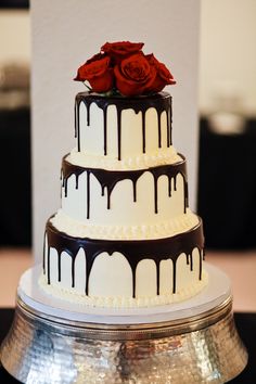 a three tiered cake with chocolate drips and red roses on top is sitting on a silver platter