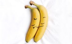 two bananas with faces drawn on them sitting side by side, one has eyes closed