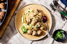 a white plate topped with meatballs covered in gravy next to a bowl of mashed potatoes