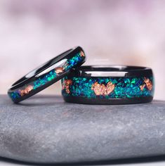 two wedding bands with blue and green opal inlays sitting on top of a rock