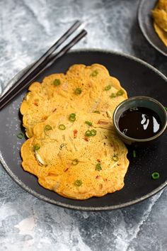 some food is on a black plate with chopsticks and sauce in the bowl