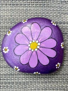 a painted rock with a flower on it, sitting on a gray cloth covered surface