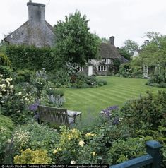 a garden with lots of green grass and flowers in front of a large white house