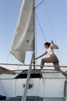 a woman is standing on the bow of a sailboat and holding her arm out