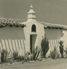 an adobe - style building with cactus and succulents in front of it