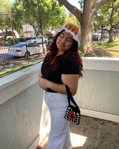 a woman with red hair wearing white pants and a sunflower hat