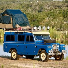 an off road vehicle parked next to a body of water with a tent on top