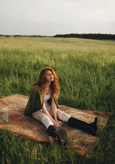 a woman sitting on top of a rug in a field