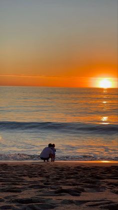 two people sitting on the beach at sunset