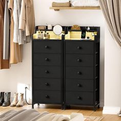 a black dresser sitting in front of a window next to a bed and clothes rack