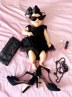 a baby doll is dressed up as a lady with black shoes and accessories on a pink sheet