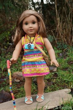 a doll with a camera and a colorful dress holding a stick in her hand while standing on a rock