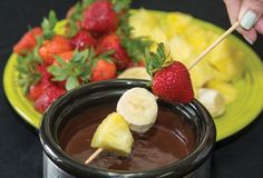 someone is dipping some fruit into a chocolate fondant with strawberries on the side