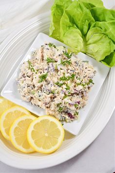 a white plate topped with salad and lemon wedges next to lettuce leaves