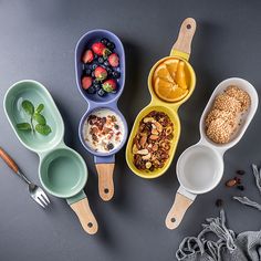 four different bowls with spoons and fruit in them on a gray surface next to other dishes