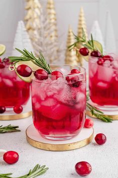 two glasses filled with cranberry punch and garnished with greenery, lemon wedges and rosemary