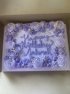 a birthday cake in a box with purple frosting and flowers on the side,