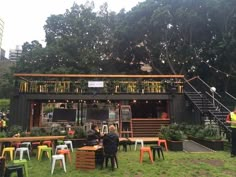 people sitting at tables in front of a building with lots of plants and lights hanging from the roof